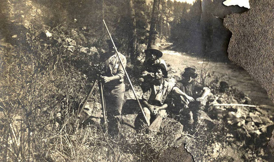 A group of men hold surveying equipment near a river.