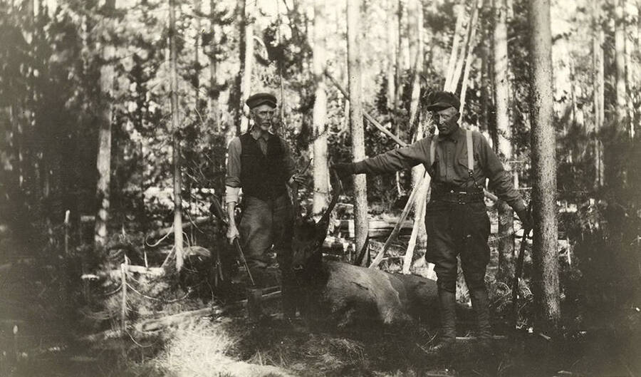Two men pose with a harested spike bull elk.