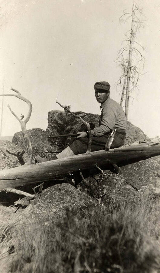 A hunter sits from a post high above the ground with a rifle waiting for elk.