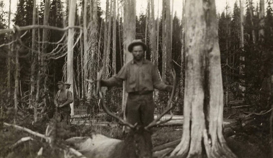 W. A. Allen Stonebraker holds the antlers of a bull elk with two other hunters in the background.