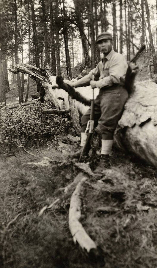 A hunter wearing a cap leans against a downed tree.