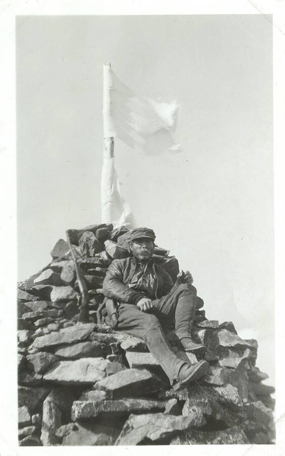 A hunter sits atop a flag-topped cairn hunting for elk.