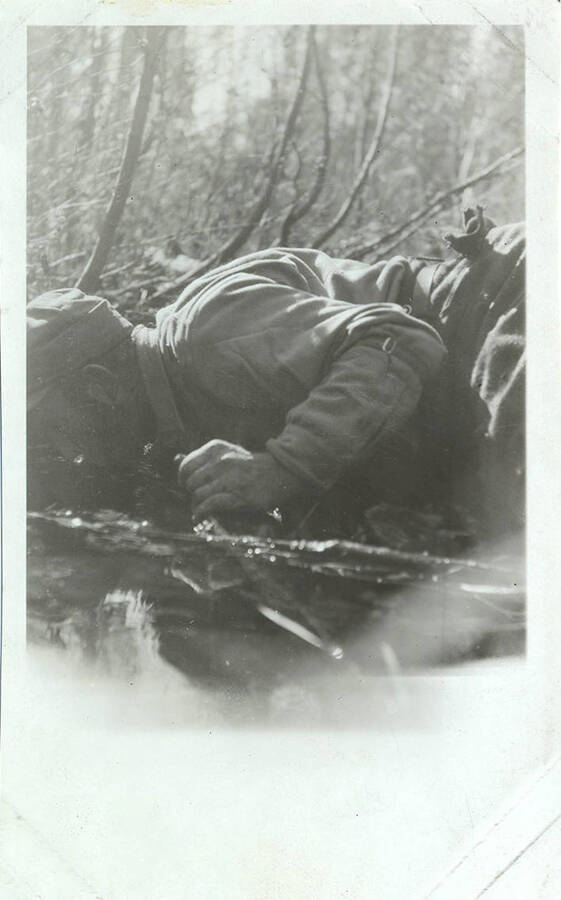 A hunter lies down to drink from a stream.