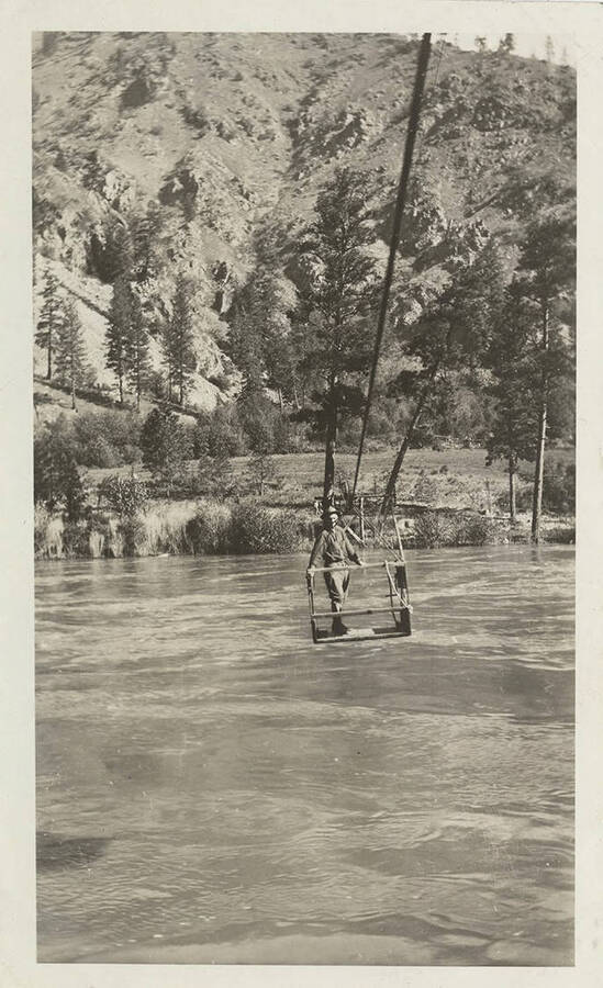 Man in cable tram basket crossing the Salmon River using a pulley.