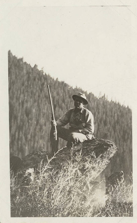 A hunter sits from a post high above the ground with a rifle waiting for elk.
