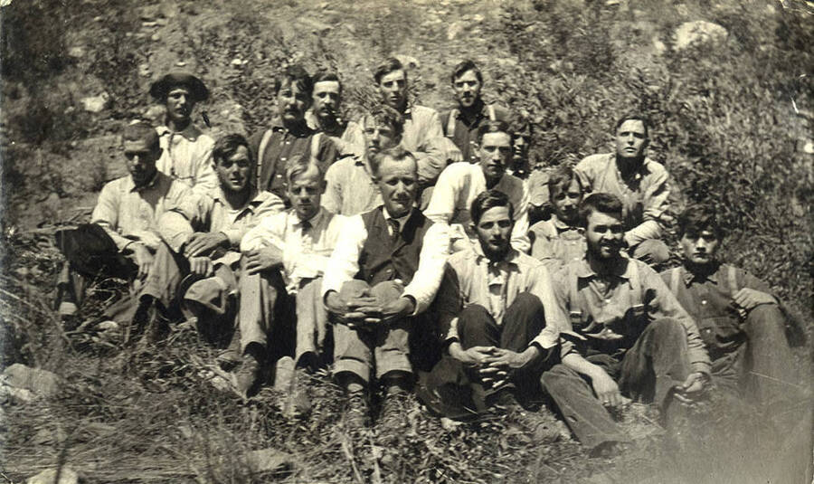 A group of men sit and pose for a photograph in a rocky area. 