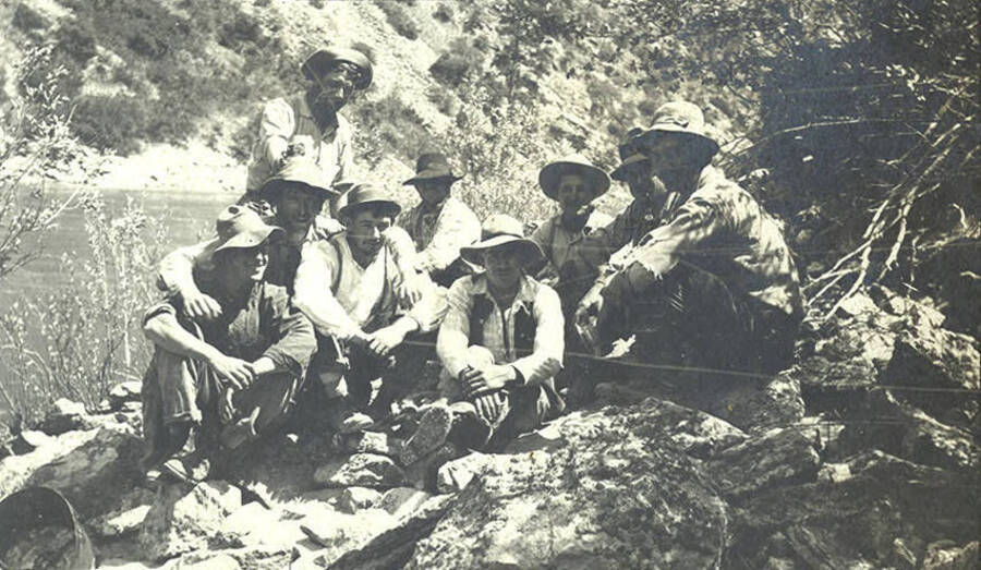 A group of men sit on rocks with a river in the background.