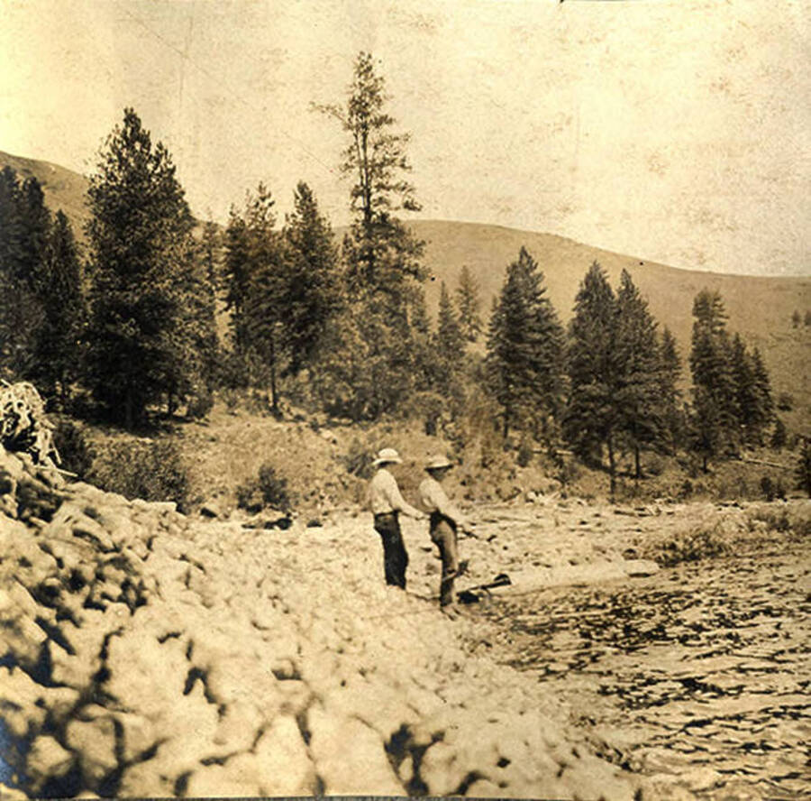Two men fishing from the bank of the Clearwater River. The photo caption reads: 'Waiting for a bite.'