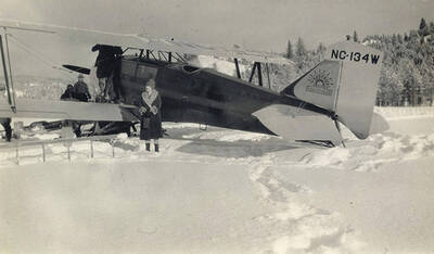 Golda Stonebraker stands in the snow beside seven passenger Zenith airplane at Stonebraker Ranch in the Chamberlain Basin. The pilot was A. A. Bennett.