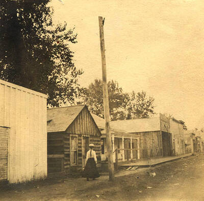 A woman walks down the main street towards the bank of Stites past smaller buildings.