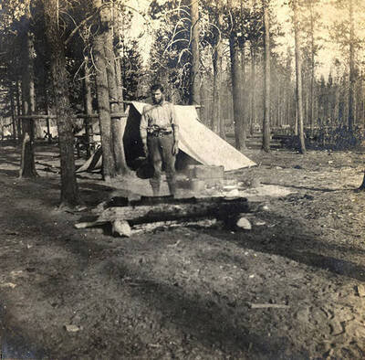A man stands near a campfire while cooking breakfast.