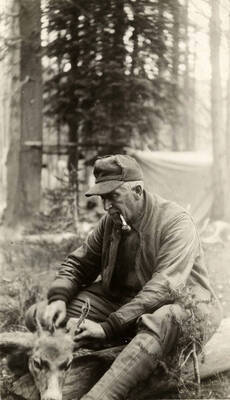 A man smokes a pipe while processing a deer.