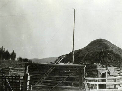 A man stands on the roof of a log cabin next to the horse corral at the Stonebraker Ranch.