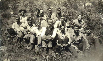 A group of men sit and pose for a photograph in a rocky area.
