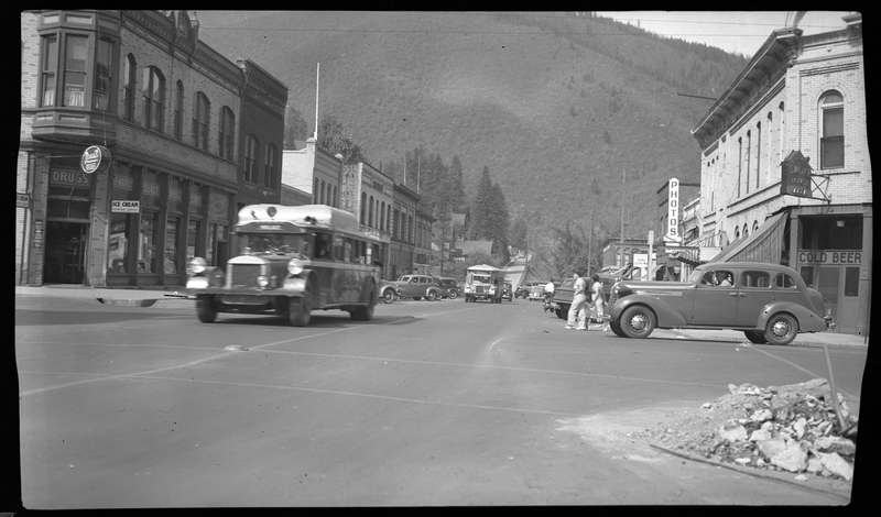 Photo of a street scene in Wallace, Idaho that includes several cars driving on the roads, people walking through the streets, and several unidentified buildings.