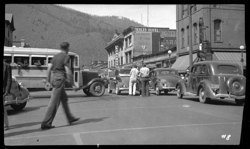 Photo of several cars and a bus lined up on the road in Wallace, Idaho, with several people around the vehicles. Buildings are visible just beyond the cars.