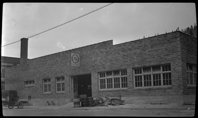 Photo of the back of a newly built Ford Garage dealership. The sign on the back reads, "Authorized Buick Service." The doors to the building are open and there is various debris on the side of the road next to the building.