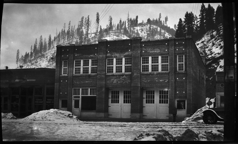 Photo of the Wallace, Idaho fire station. There is snow on the ground in front of the building, and a car driving past.