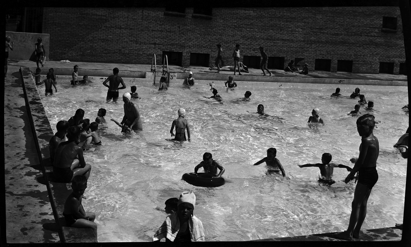 Photo of a large number of people swimming in the Wallace, Idaho Swimming Pool. There are people on the concrete outside of the pool, but a majority of people are actively swimming.