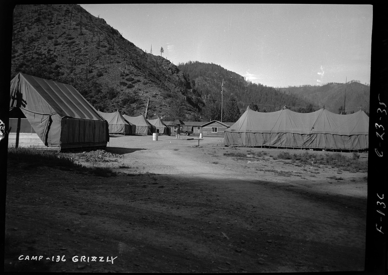 Photo described as "Civilian conservation corps camps during the 1930s, Shoshone County," with Camp-136-Grizzly written on the negative. Several tents and a building are visible in a clearing of a forest.