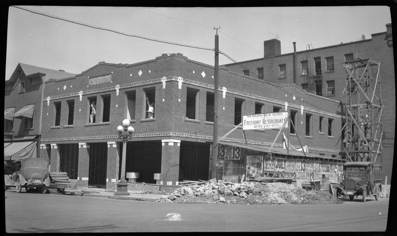 Photo of the Hale Building under construction. There is a large sign next to the building that reads "This building will be occupied; Fremont Restaurant; After July 1st." There are several cars parked on the road next to the building, and a large pile of debris that is likely from the construction.