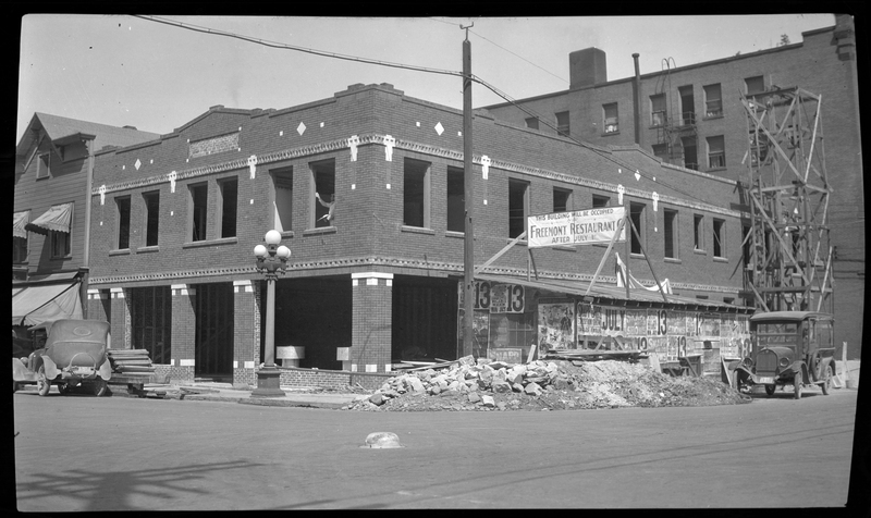 Photo of the Hale Building under construction. There is a large sign next to the building that reads "This building will be occupied; Fremont Restaurant; After July 1st." There are several cars parked on the road next to the building, and a large pile of debris that is likely from the construction.