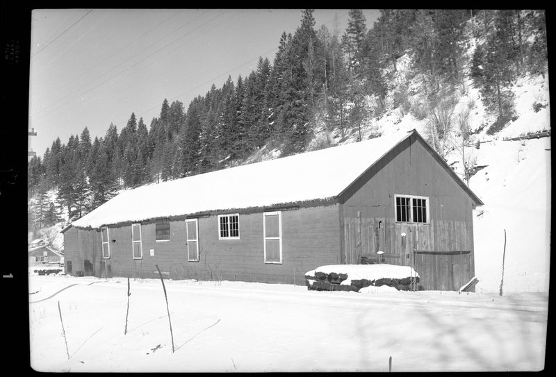 Photo of an unidentified building in the snow. Described as "Standard Dairy, E. F. Gentry." The building's roof and the ground surrounding it are covered in snow, and trees are visible on the hill directly behind the building.