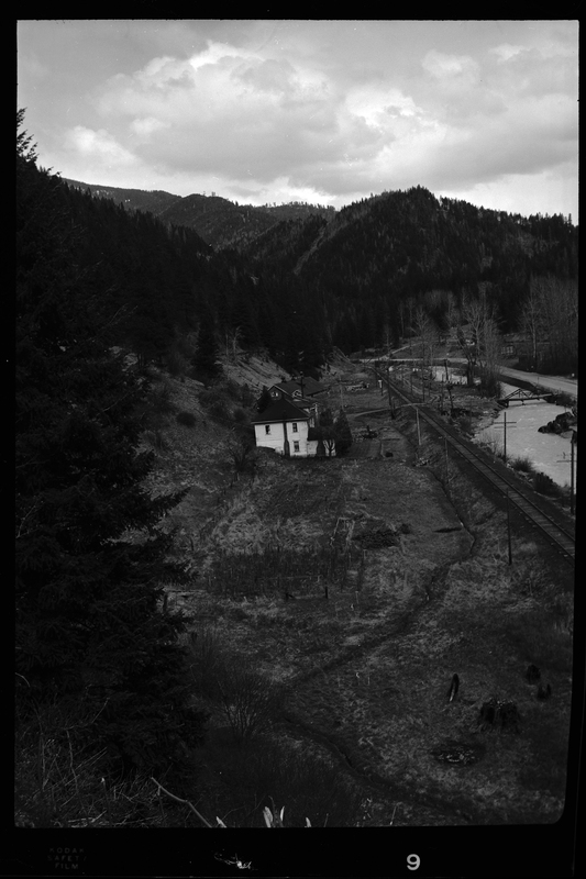 Photo of what appears to be a house in the distance. Described as "Standard Dairy, E. F. Gentry." The photo was taken from a higher elevation and looks down at the building from the side. There is a river that runs near by the building.