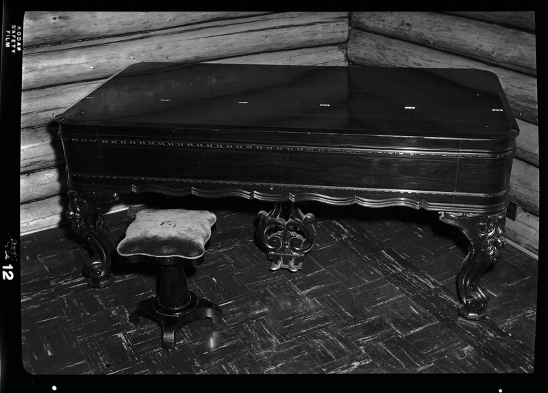 Photo of a Chickering and Sons square Grand Piano in the Stansfield house. The top of the piano is closed and the keys are covered.