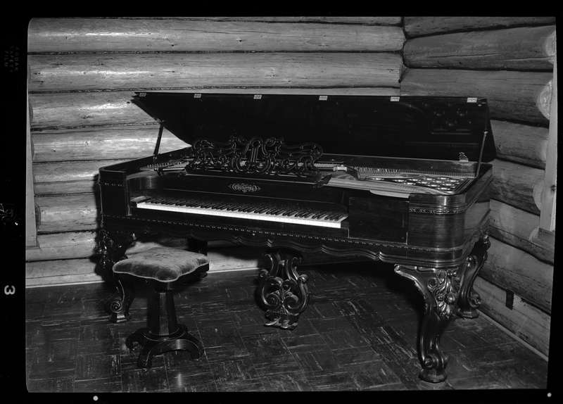 Photo of a Chickering and Sons square grand piano in the Stansfield house. The top of the piano is lifted open and the keys are visible, and there is a single seater piano bench in front of it.