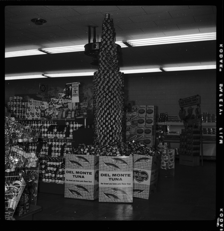 Photo of the Del Monte Tuna display inside of a grocery store. The tuna is stacked in the shape of a tower that nearly reaches the ceiling, and there are tall boxes of the canned tuna surrounding it. Other canned and boxed food items are visible in the background.