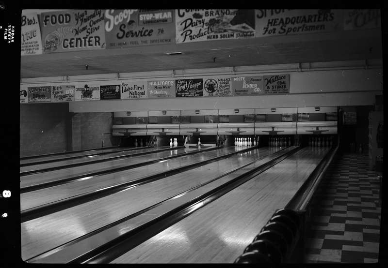 Photo of the six bowling lanes at Albi's Bowling Alley. Five of the lanes have all their pins standing, and one lane has two pins standing. There are poster advertisements all over the walls.