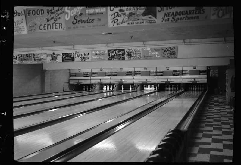 Photo of the six bowling lanes at Albi's Bowling Alley. Four of the lanes have all their pins standing, one lane has just one pin standing, and another has five pins standing. There are poster advertisements all over the walls.