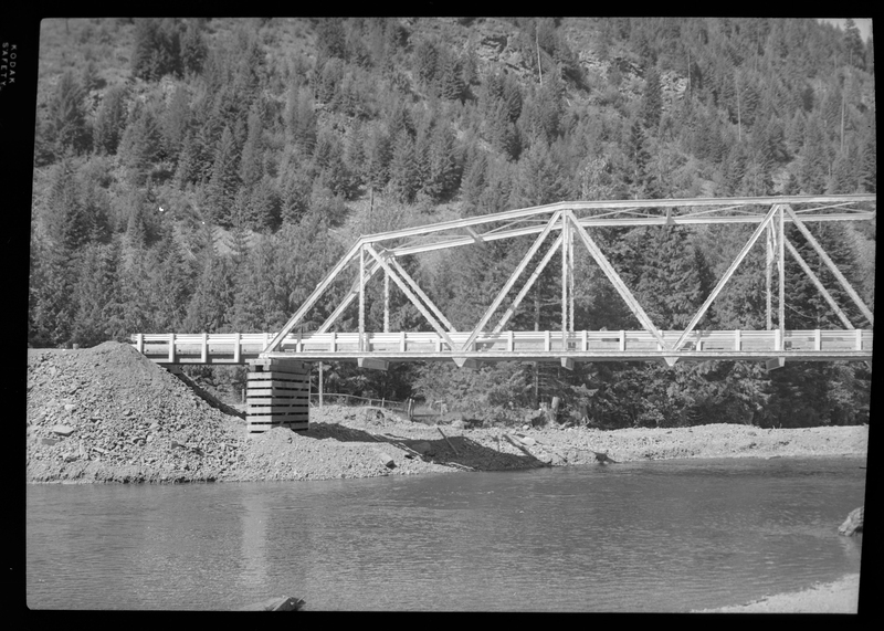 Photo of the ongoing construction of the Pritchard Bridge in Pritchard, Idaho. The bridge frame is in place over the river and settled on the bases.