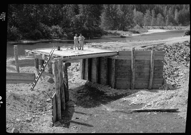 Photo of the ongoing construction of the Pritchard Bridge in Pritchard, Idaho. This is likely the construction of the base of the bridge, which two men are standing on top of.