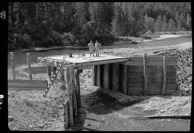 Photo of the ongoing construction of the Pritchard Bridge in Pritchard, Idaho. This is likely the construction of the base of the bridge, which two men are standing on top of.