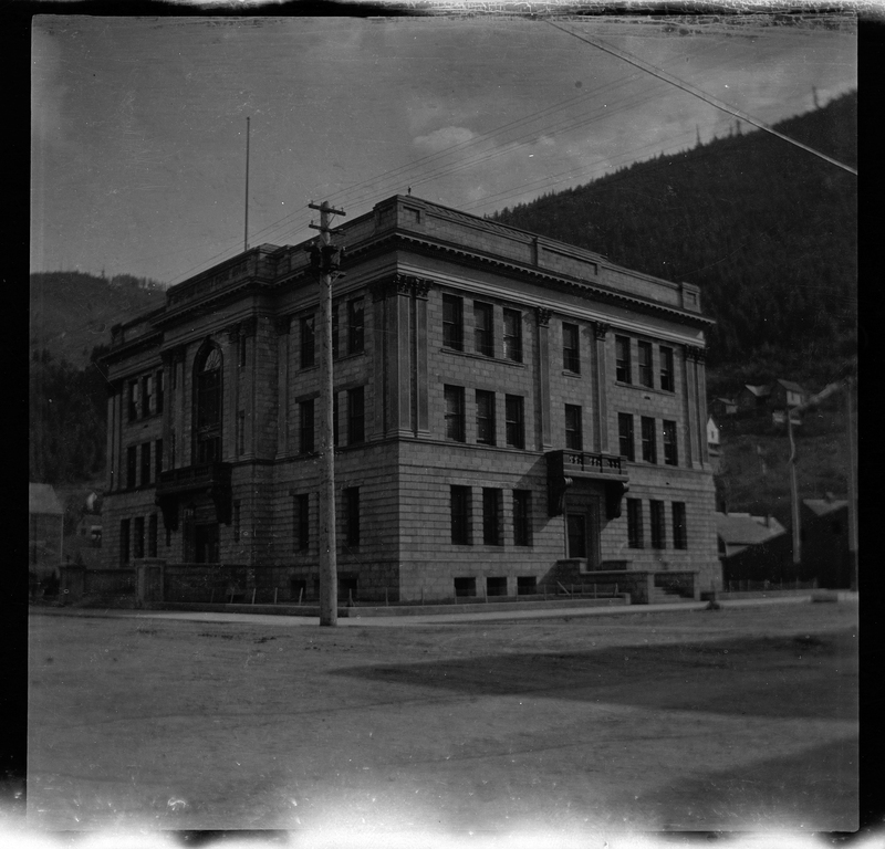 Photo of a Courthouse building. The building is on the street corner and the photo was taken from the opposite street corner, showing two sides of the building. The negative is slightly damaged.