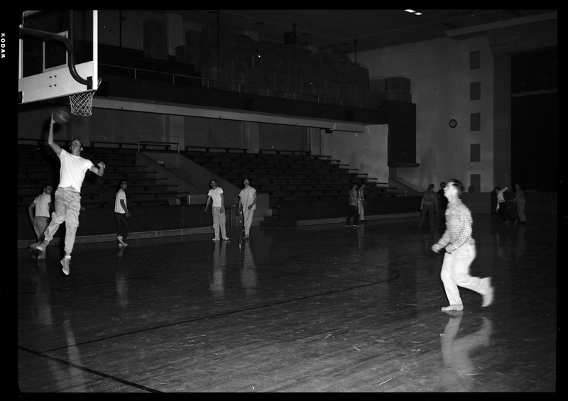 A group of people, likely all men, are playing a game of basketball at the Civic Auditorium in Wallace, Idaho. They are all wearing street clothes, not uniforms.