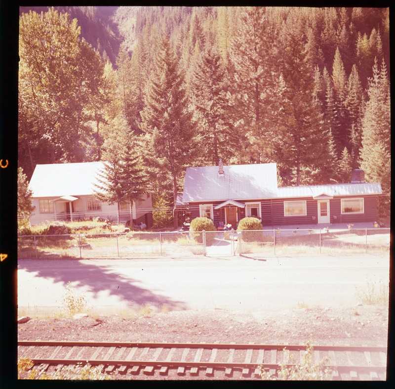 Color photo of two houses on A. A. M. Arnold's property on Highway 10. Both houses appear to be one story tall and they are surrounded by trees. There is a railroad track between the houses and the photographer.