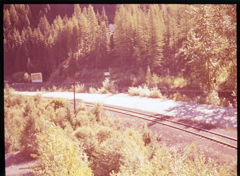 Color photo of the road near A. A. M. Arnold's property on Highway 10. There are two signs in the distance but details cannot be made out. There is a railroad between the road and the photographer, and the whole area is surrounded by trees.