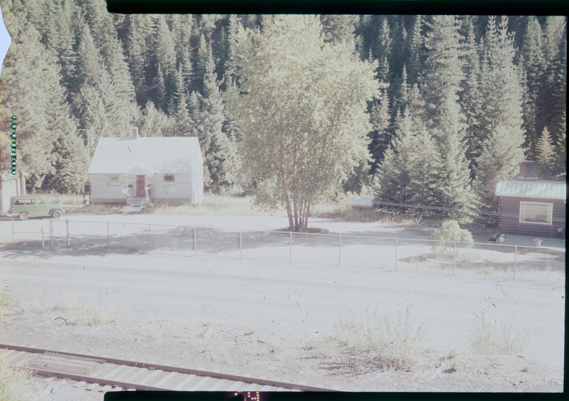 Color photo of a house and a tree on A. A. M. Arnold's property on Highway 10. There is another building to the right of the tree that is mostly out of frame from the picture. A railroad track runs on the ground between the photographer and the house.