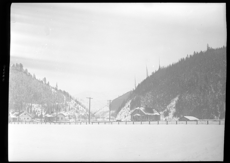 Photo of the city of Silverton, Idaho in the snow. Several houses are visible, all covered and surrounded by snow. The mountains behind the city are covered in trees and snow.