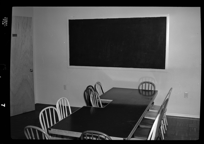 Photo of a desk surrounded by chairs in a room within an Episcopal church in Wallace, Idaho. There is a blackboard against the wall behind the desk and chairs.