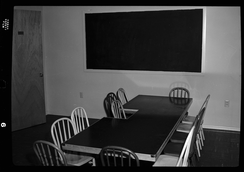Photo of a desk surrounded by chairs in a room within an Episcopal church in Wallace, Idaho. There is a blackboard against the wall behind the desk and chairs.