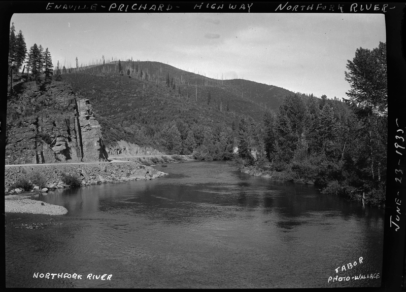 Photo of the North Fork of the Coeur d'Alene River and the Enaville-Prichard highway. The highway winds against the river on the left, and on the right side of the river the ground is covered in trees.