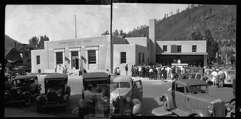 Photo of a crowd of people standing next to the Wallace Post Office building. Two negatives are taped together for this photo, showing the building in its entirety. Several cars are parked around the area and a man can be seen addressing the crowd.