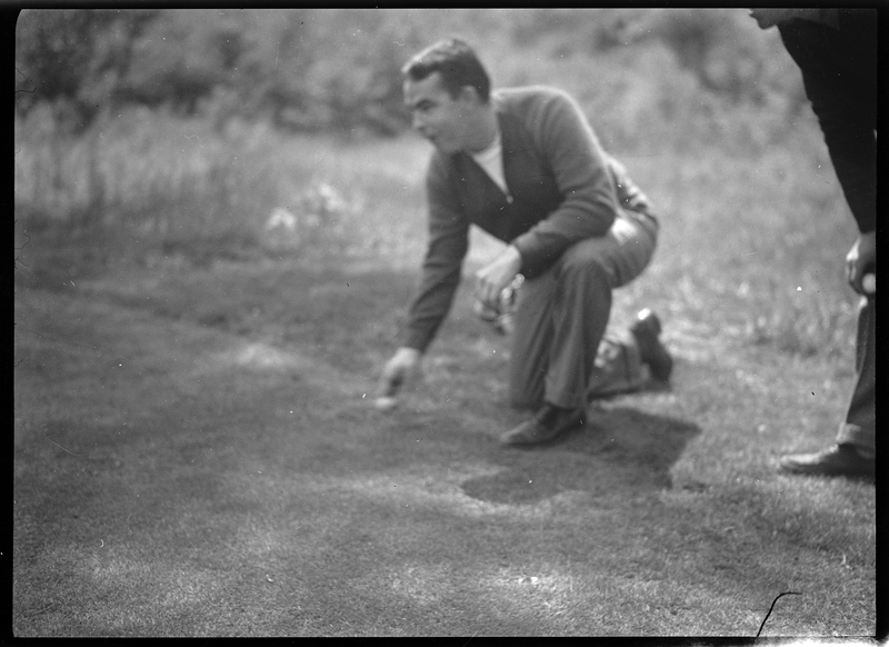 Photo of an unidentified man playing golf at Shoshone Golf Course. The man is knelt on the ground and holding a golf ball in his hand.
