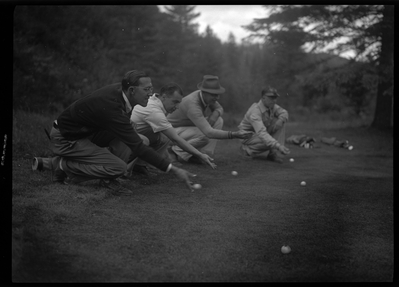 Photo of four unidentified men kneeling on the ground while rolling golf balls on the ground at the Shoshone Golf Course.