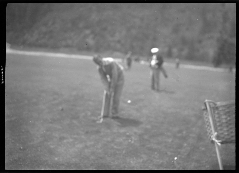 Photo of an unidentified man playing golf at Shoshone Golf Course. The photo is out of focus, but the general shape of a man holding a golf club can be made out, as well as other people in the background.