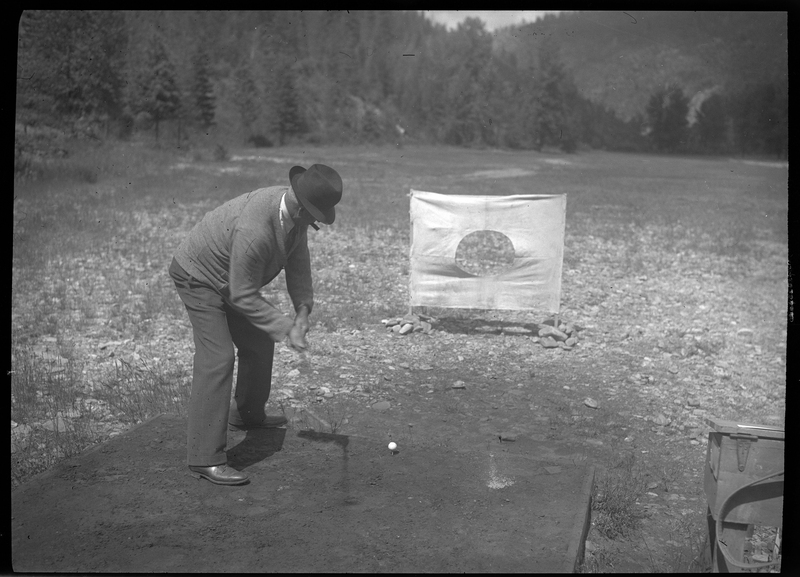 Photo of an unidentified man playing golf at Shoshone Golf Course. The man is leaning over and preparing to hit a golf ball at a target a few feet away. The golf club is not visible in the man's hands, but the shadow of it can be seen on the ground.